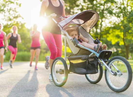 Woman pushing her toddler while running in nature with friends